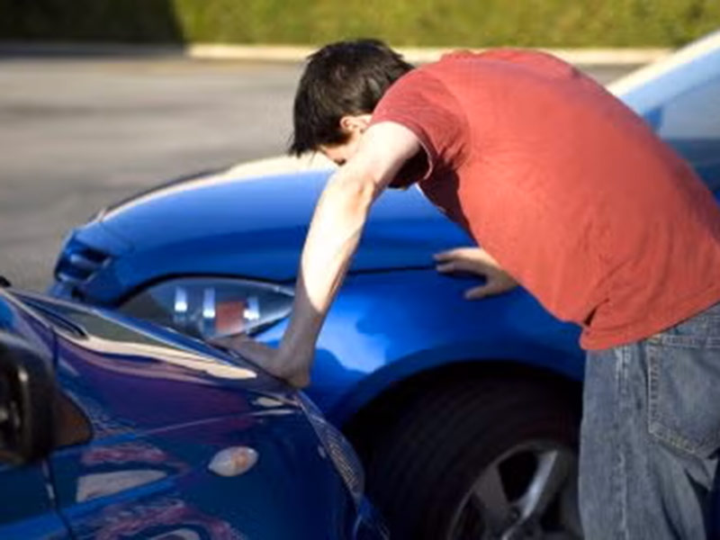A man leans over a blue car in Tracy, CA, highlighting Auto Accident Claims.